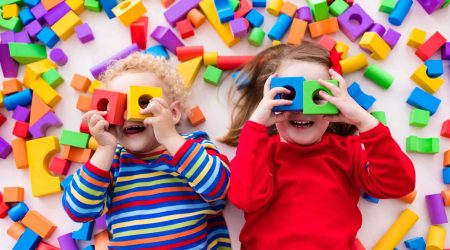 Happy preschool age children play with colorful plastic toy blocks. Creative kindergarten kids build a block tower. Educational toys for toddler or baby. Top view from above.